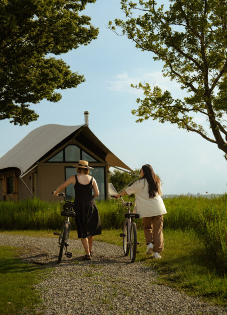 Two women pushing bikes toward a cabin tent